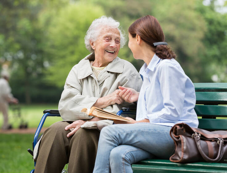 Une dame agée et une aide-soignante discutent sur un banc